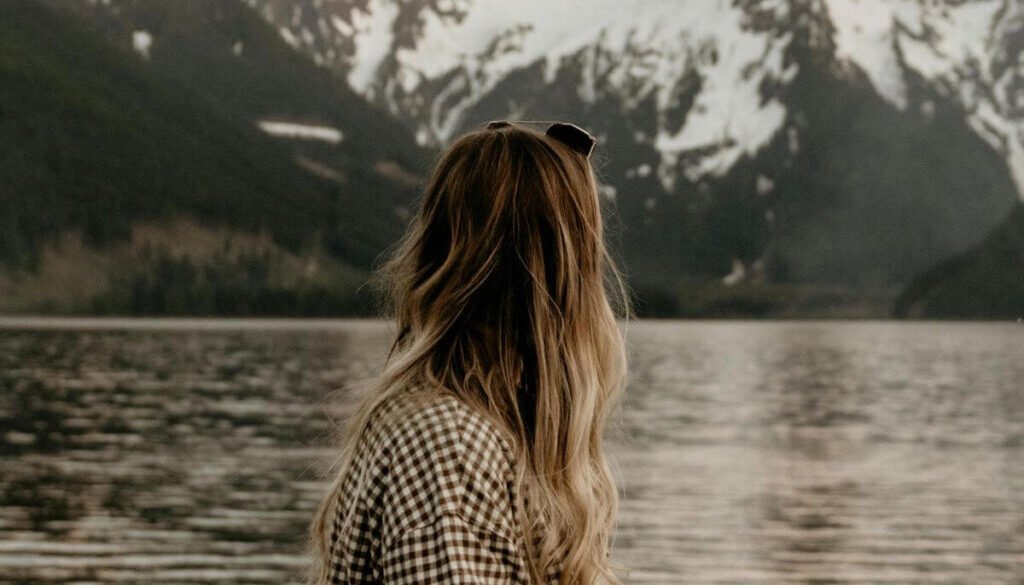 Christian woman standing by a lake in quiet reflection, symbolizing prayer and learning how to hear God’s voice.