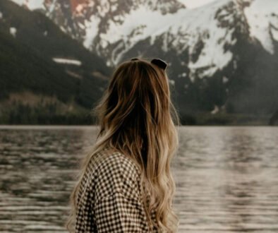 Christian woman standing by a lake in quiet reflection, symbolizing prayer and learning how to hear God’s voice.