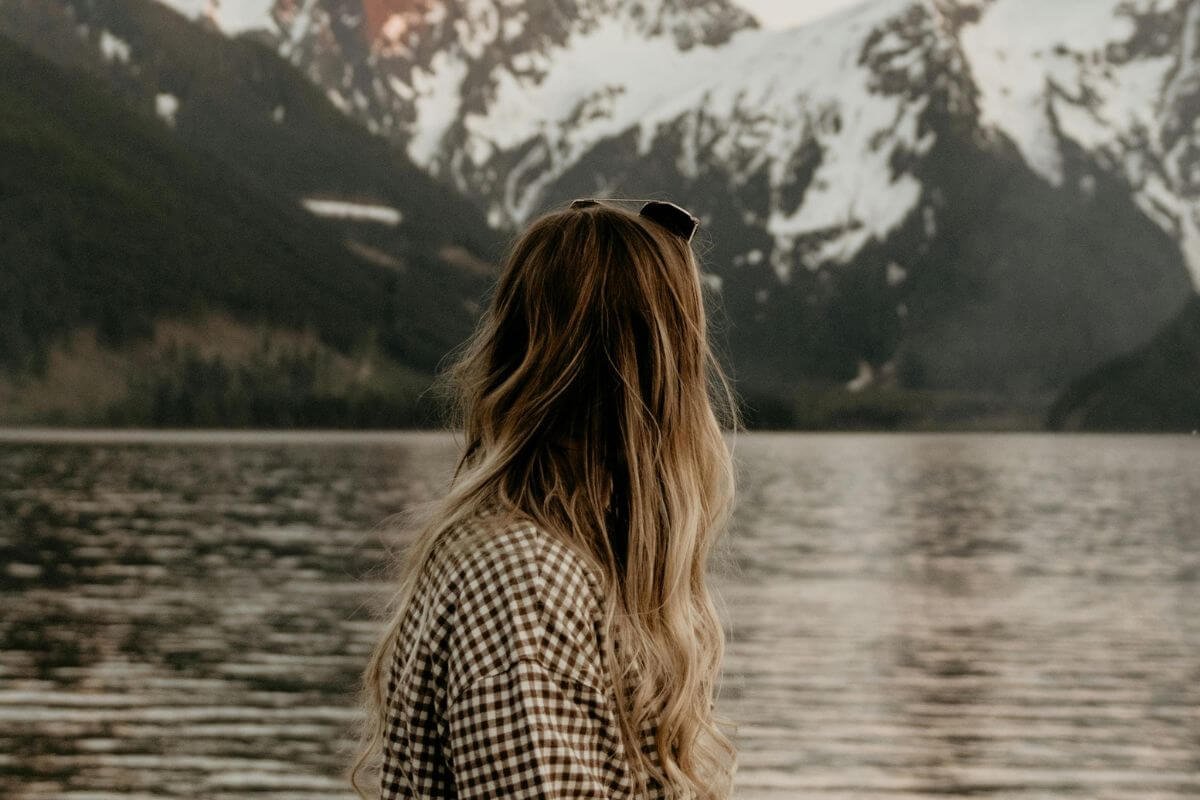 Christian woman standing by a lake in quiet reflection, symbolizing prayer and learning how to hear God’s voice.