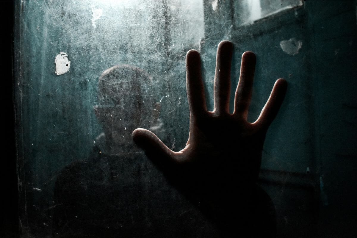 Person standing behind fogged glass with hand pressed against it, representing Elijah and depression and emotional isolation