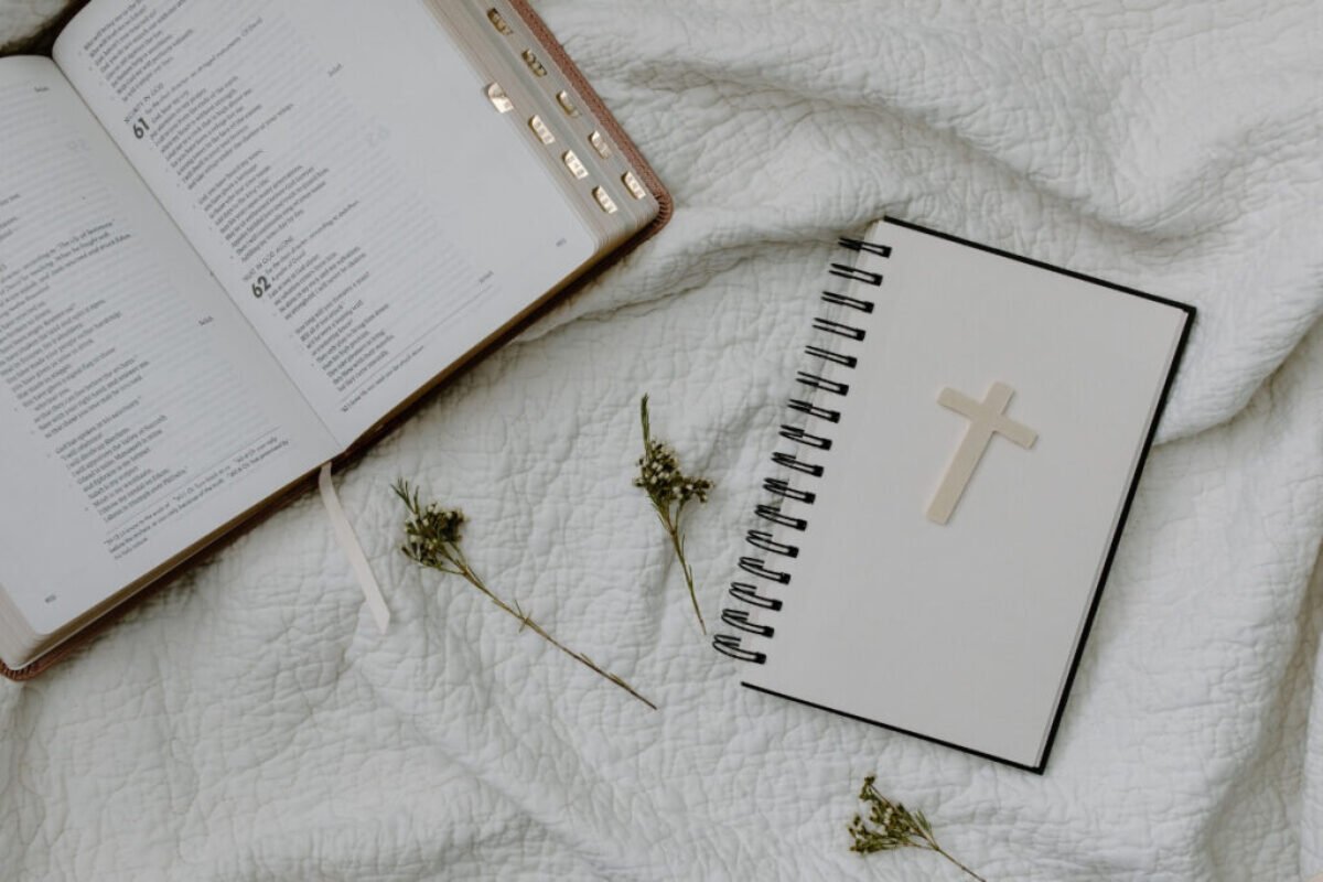 Open Bible and cross notebook on white fabric with dried flowers