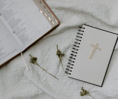 Open Bible and cross notebook on white fabric with dried flowers