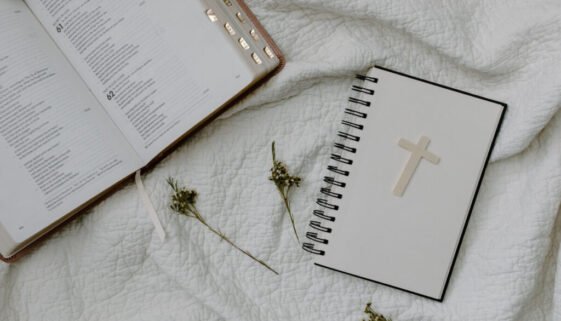 Open Bible and cross notebook on white fabric with dried flowers