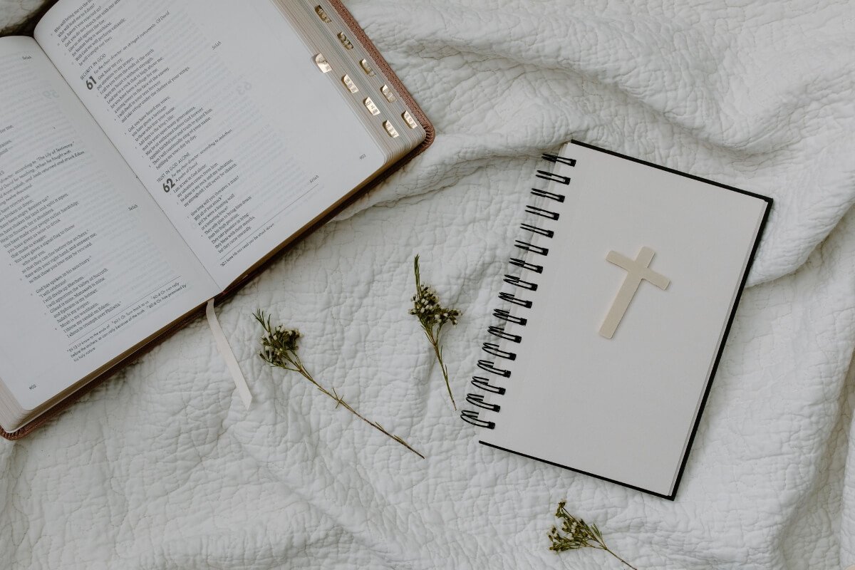 Open Bible and cross notebook on white fabric with dried flowers